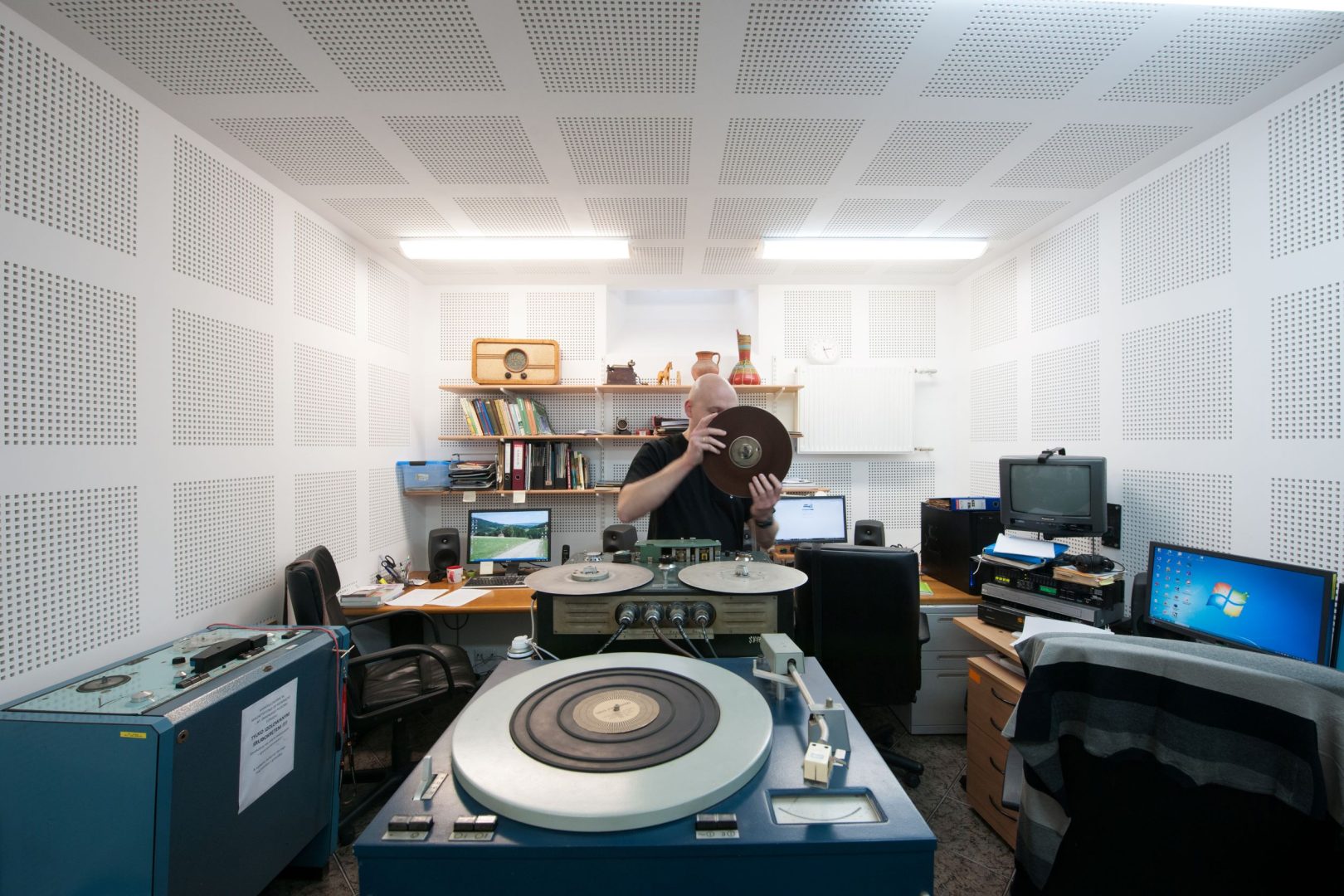 Mężczyzna w wygłuszonym studiu podnosi płytę gramofonową