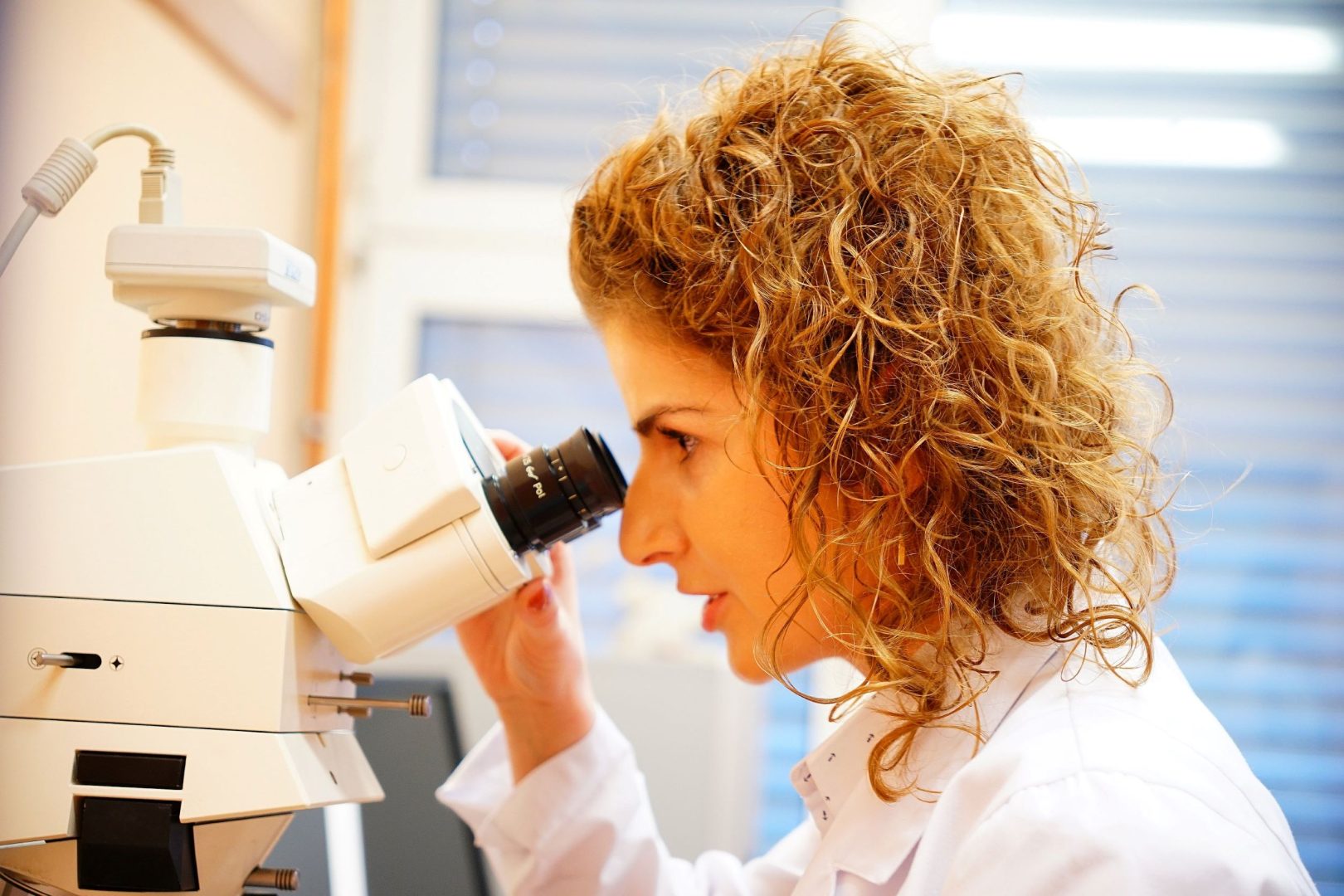 Kobieta o kręconych włosach spogląda przez mikroskop