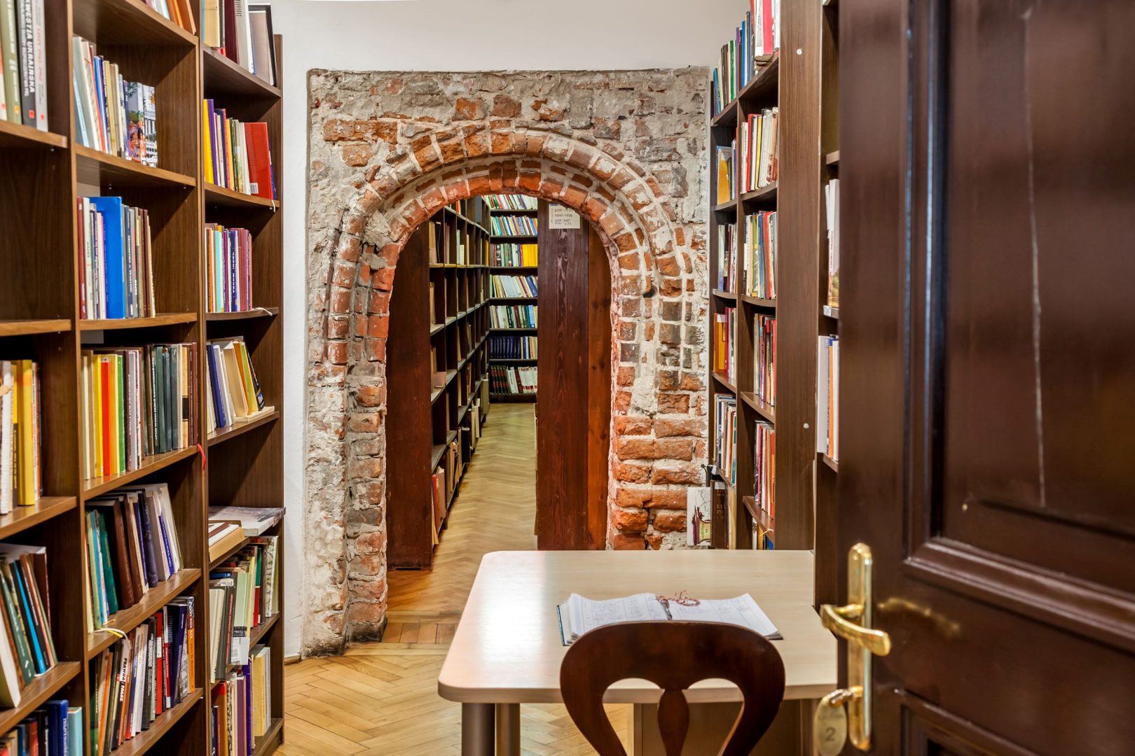 Przejście między regałami z książkami, w środku ceglany portal, pod którym przechodzi się do dalszych pomieszczeń