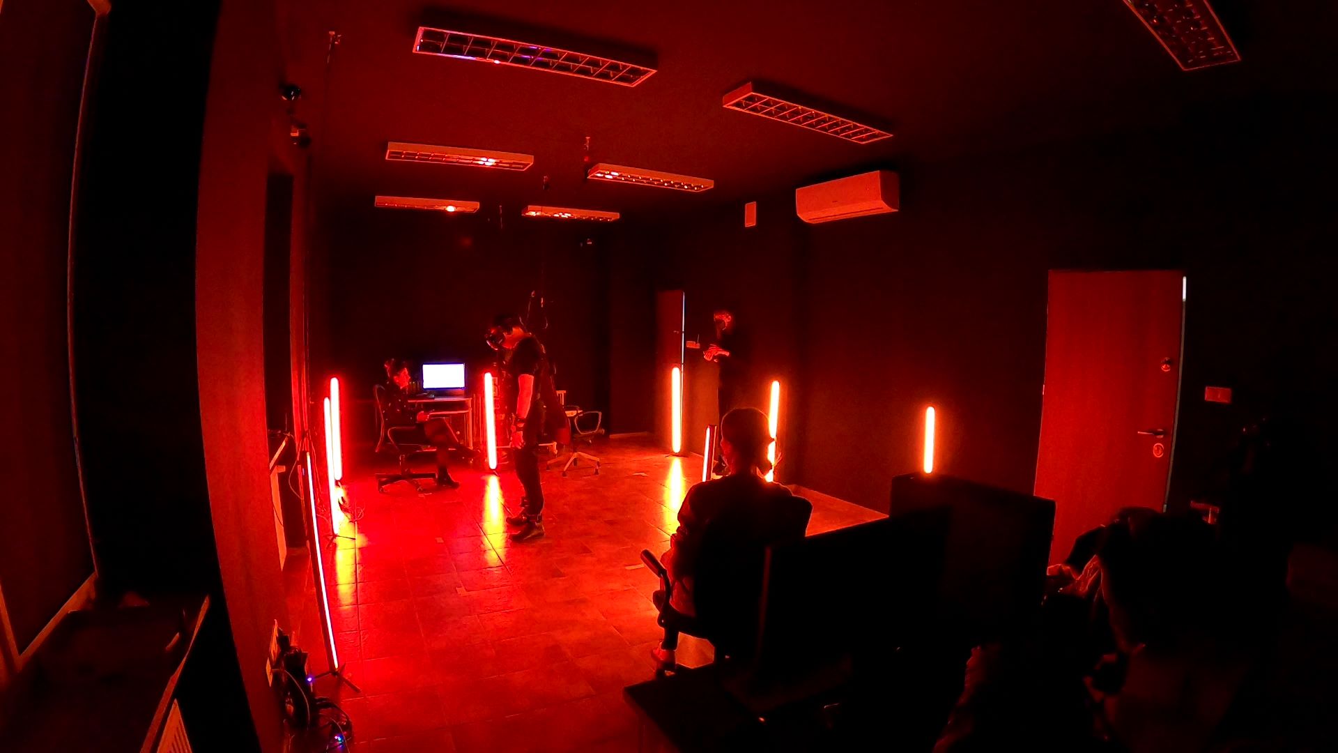 Podświetlony na czerwono pokój, w nim osoba w okularach do obserwacji wirtualnej rzeczywistości