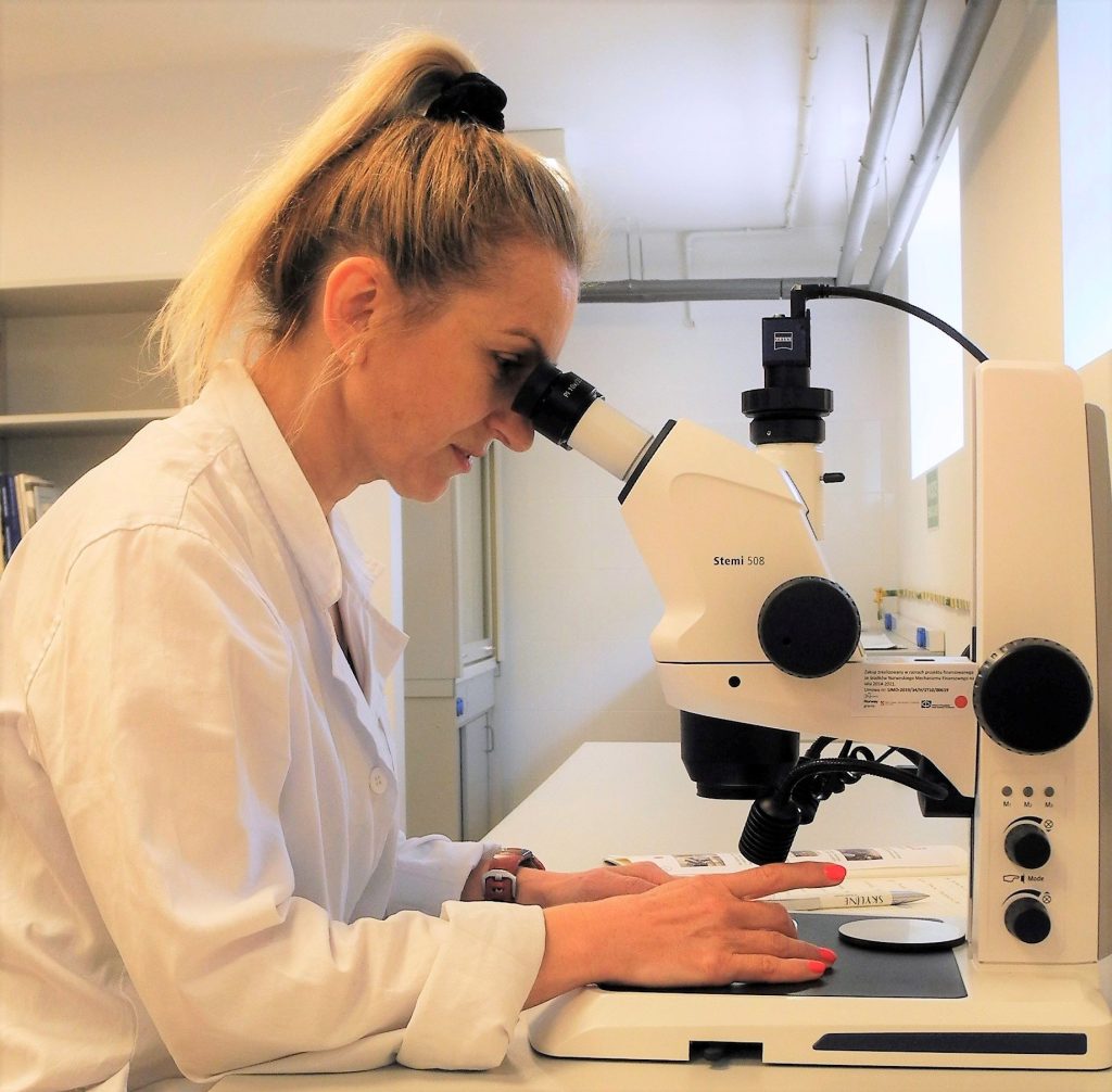 Kobieta w białym fartuchu patrzy przez mikroskop