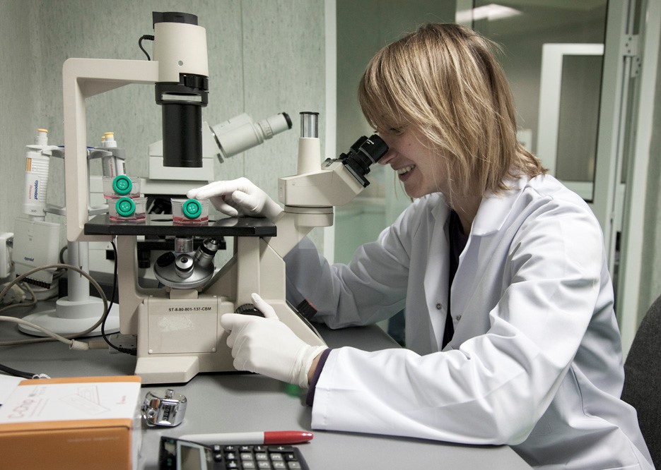 Kobieta w białym fartuchu i rękawiczkach obsługuje mikroskop