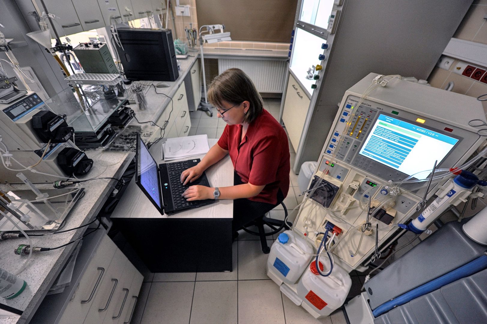 Kobieta w czerwonej koszulce pracuje na laptopie w laboratorium