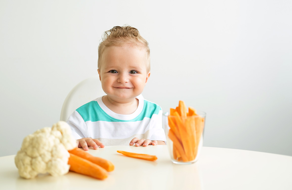 Dziecko siedzące przy stole, na którym znajdują się warzywa